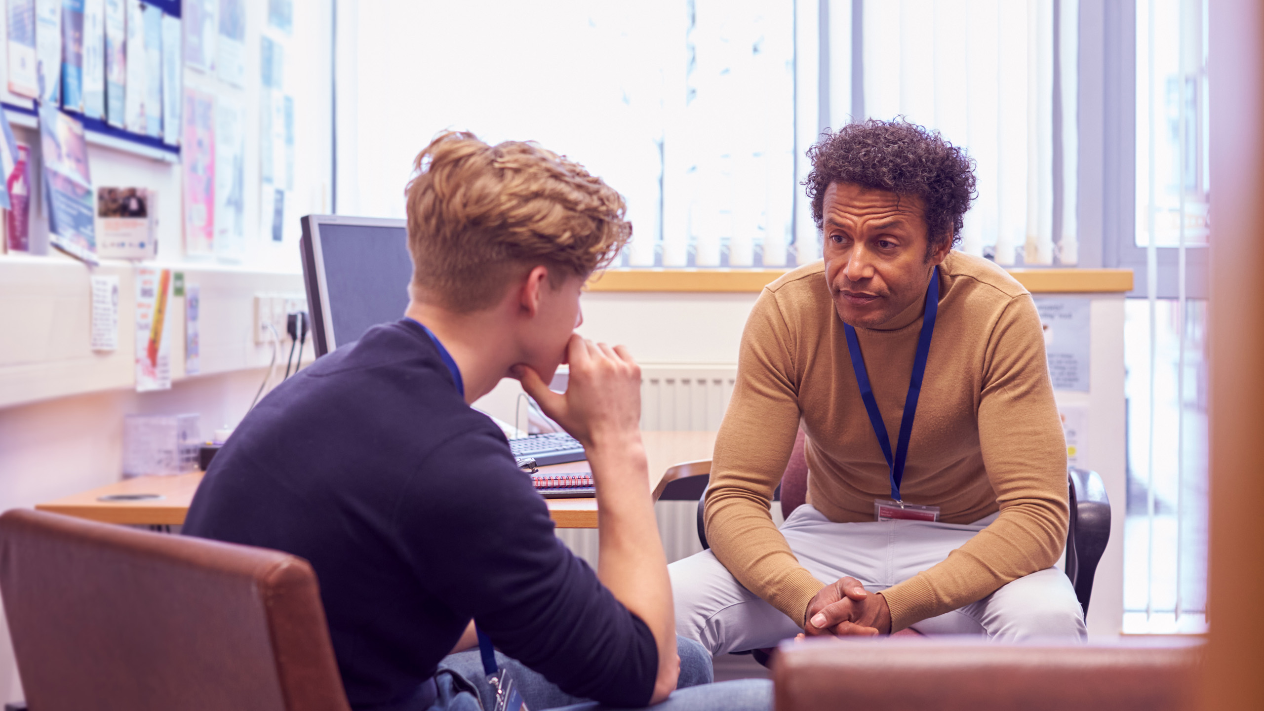 A student talking to a teacher while the teacher listens, both are sat down.