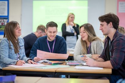 Four adult students smiling and working on a group project.